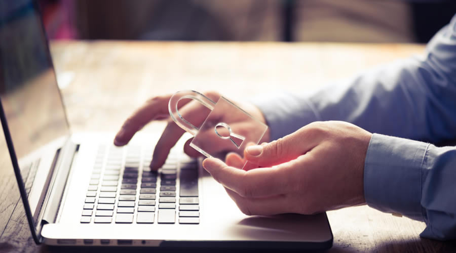 Am Laptop arbeitende Hände, eine Hand hält Glasschloss