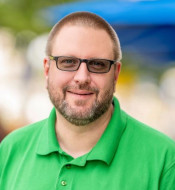 Torsten Hallmann, mit grauen Haaren und Bart, trägt ein grünes Polohemd und Brille, lächelt frontal zur Kamera.