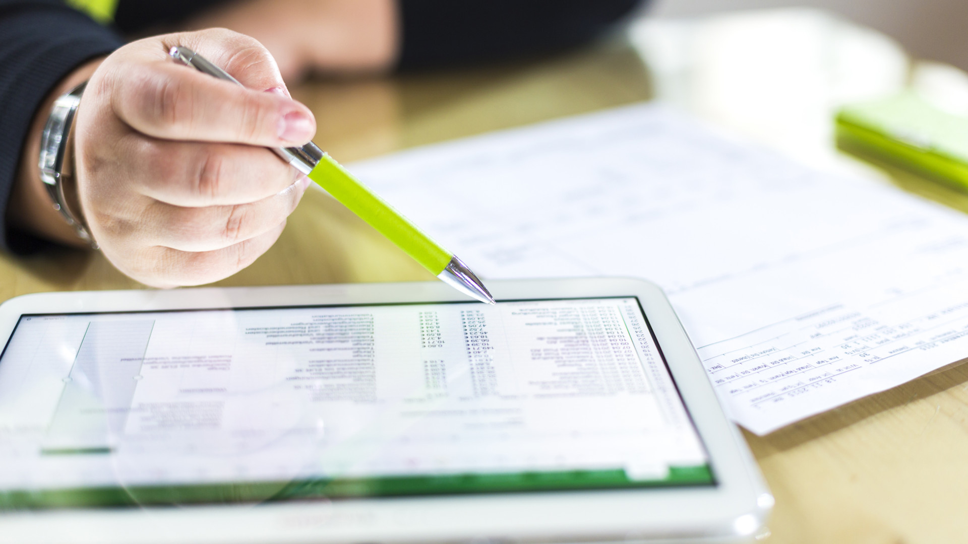 Person sitzt vor einer Rechnung vor Papier und einem Tablet