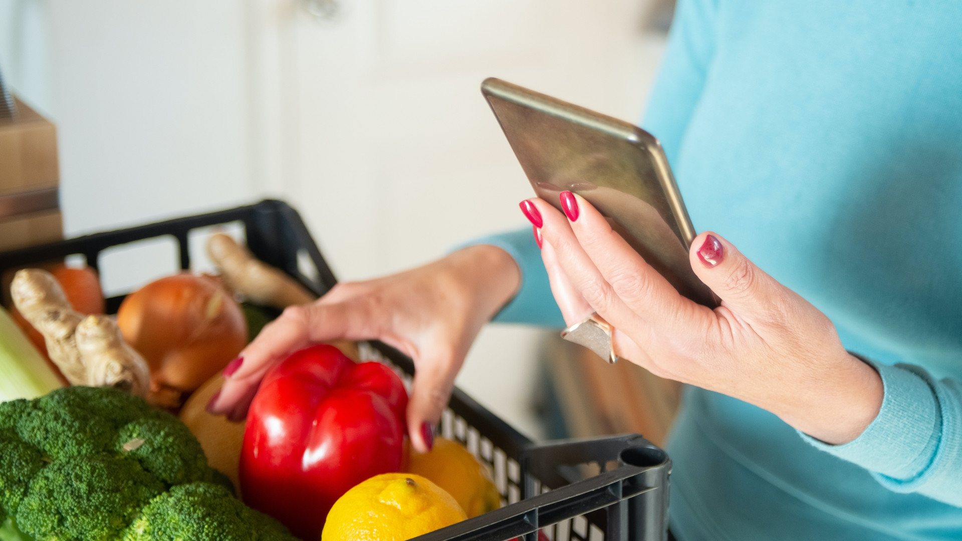 Frau mit Smartphone und Einkaufskorb gefüllt mit Obst und Gemüse
