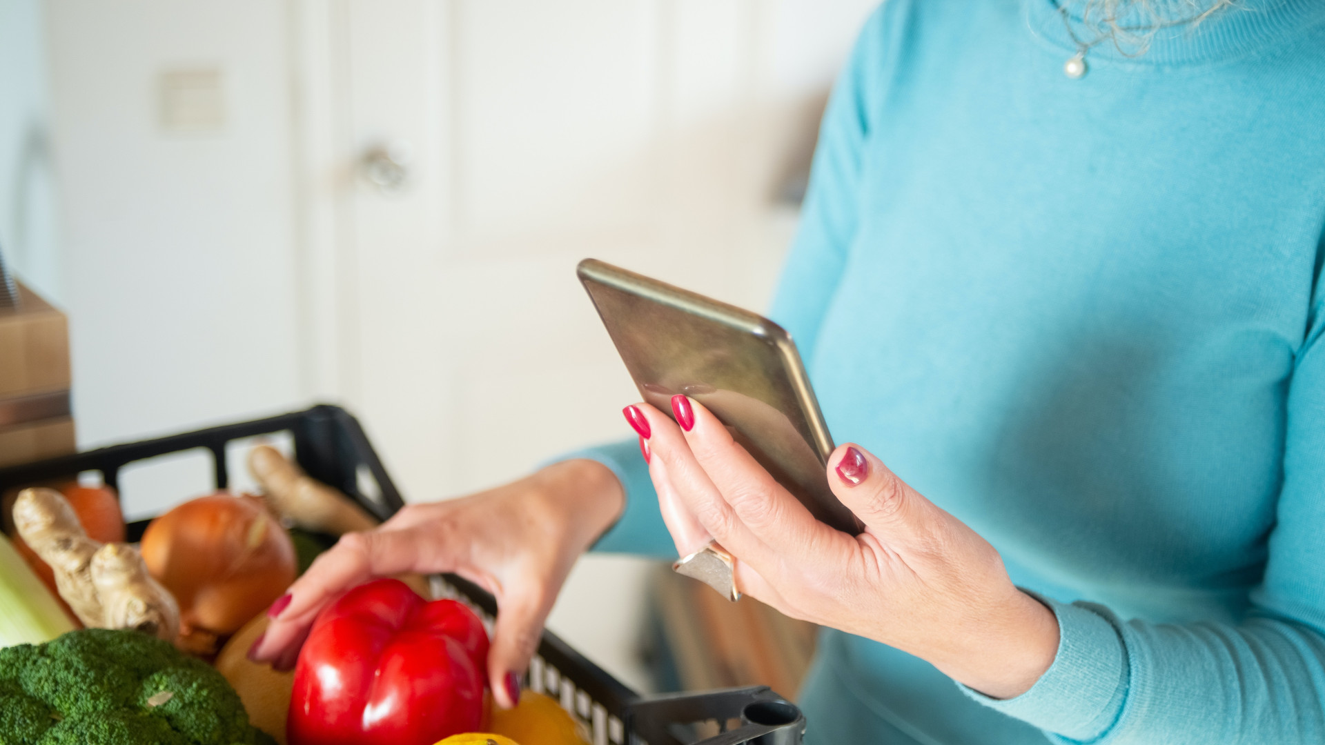 Frau mit Smartphone und Einkaufskorb gefüllt mit Obst und Gemüse