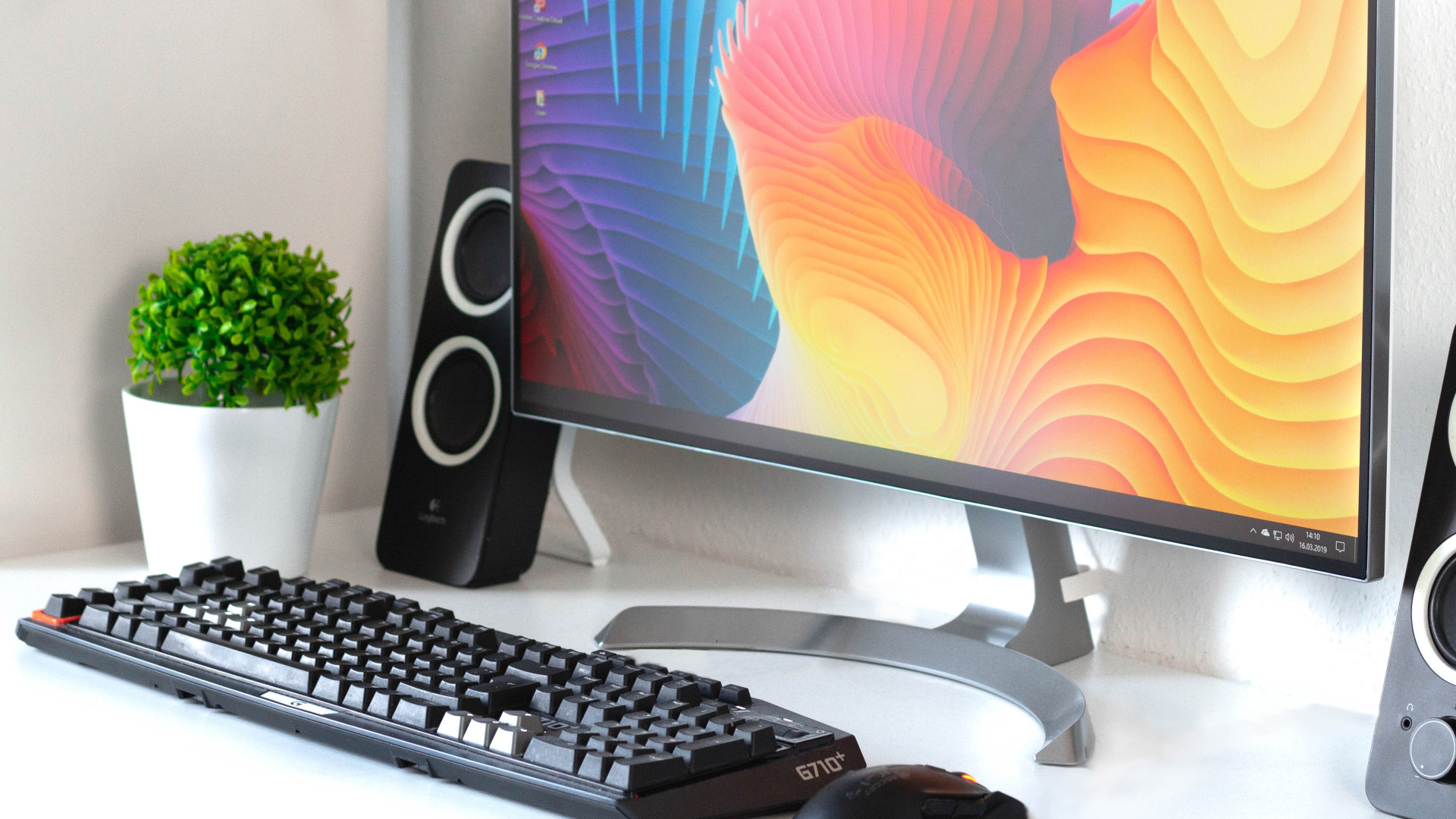 Computerarbeitsplatz mit Monitor, Lautsprechern, Tastatur, Maus und Sci-Fi-Figur auf einem weißen Tisch.