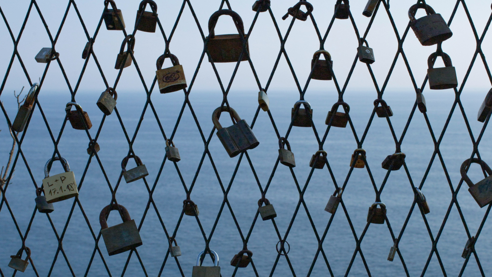 Schlösser an Maschendrahtzaun mit Blick aufs Meer