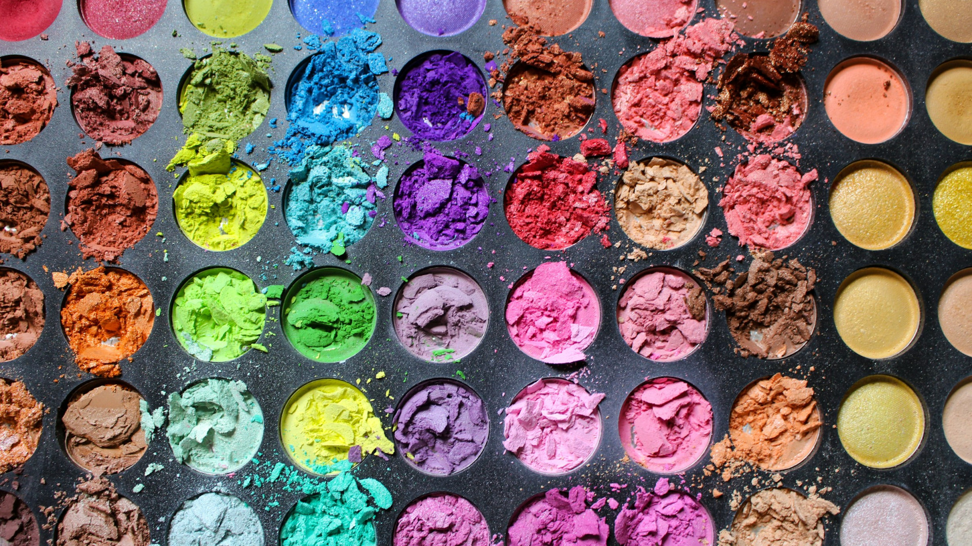 Eine Palette mit einer Vielzahl kreisförmiger Lidschatten in verschiedenen Farben, von kräftigen Rottönen über Blau, Grün, Gelb, Lila bis hin zu Erdtönen und Gold.