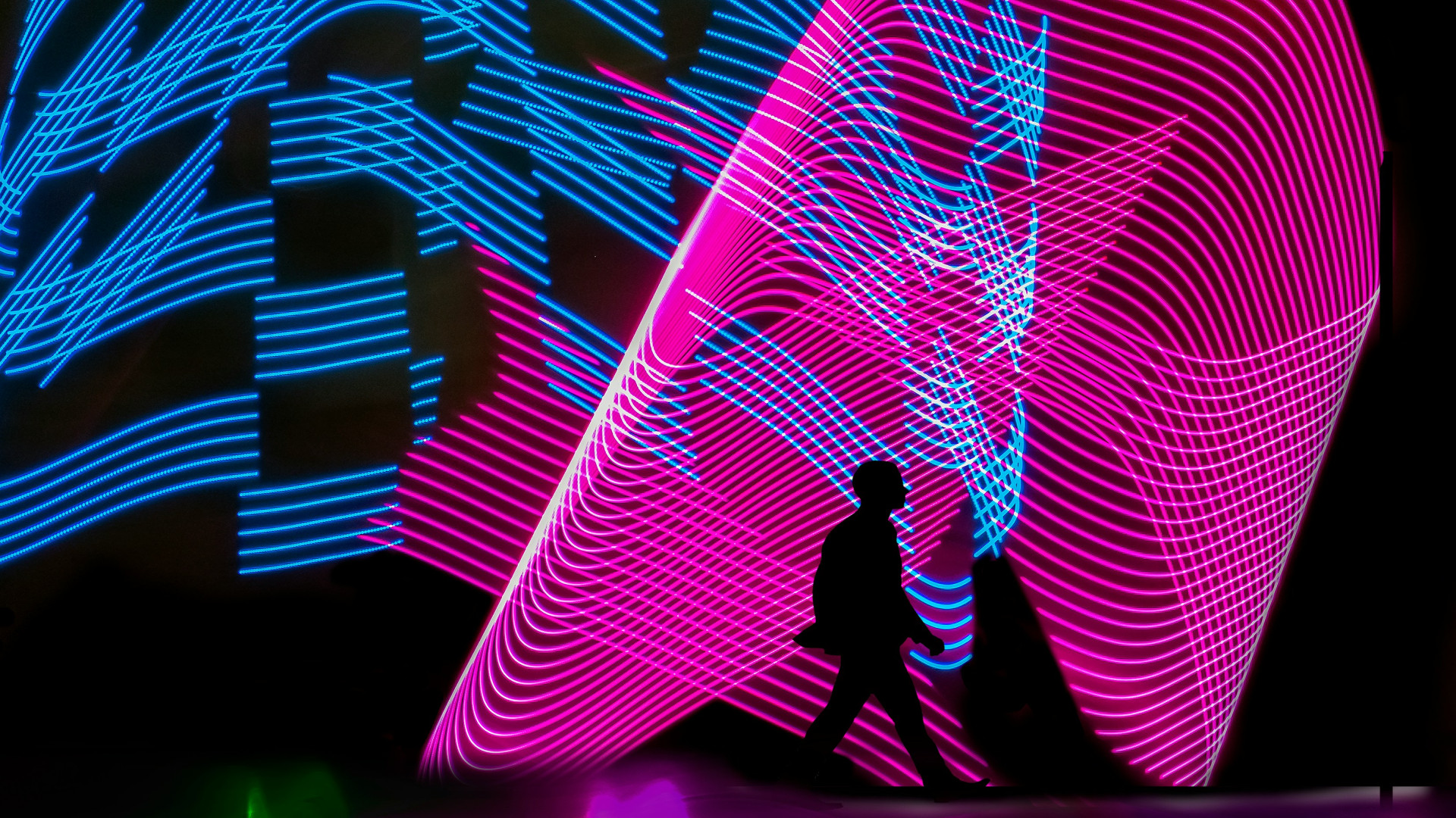 Das Bild zeigt eine männliche Silhouette von der Seite vor einem abstrakten Hintergrund aus neonblauen und -pinken Leuchtstreifen, die wellenförmig den Hintergrund nahezu vollständig ausfüllen. Der Mann ist nach rechts gewandt und läuft in dieselbe Richtung.