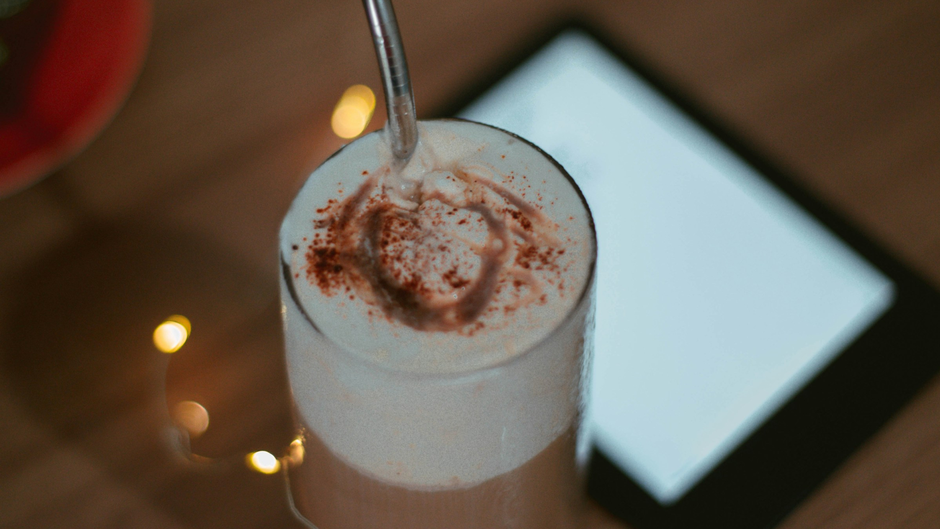 Ein Glas Latte mit Milchschaum steht im Vordergrund auf einem Holztisch. Im Hintergrund ein verschwommenes E-Book.