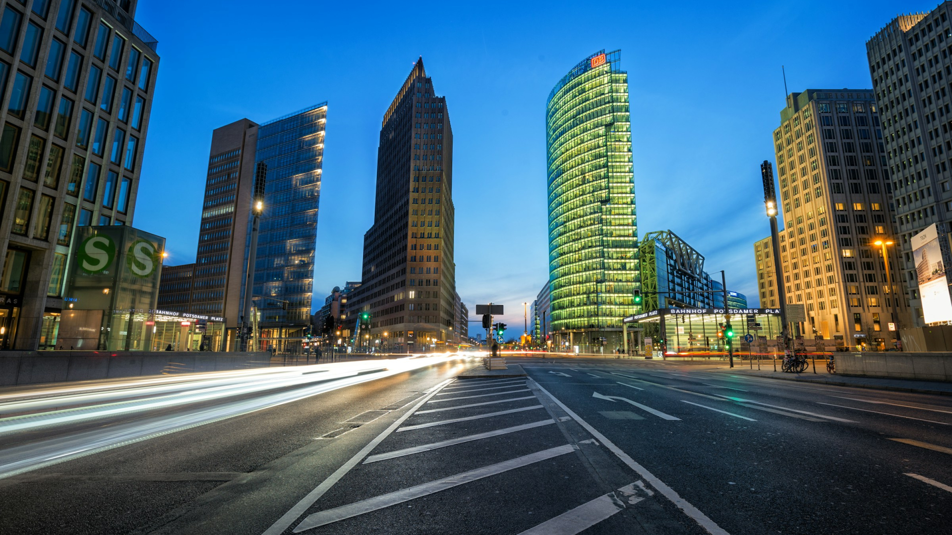 Abendaufnahme vom Potsdamer Platz mit beleuchteten Hochhäusern und Lichtspuren fahrender Autos.