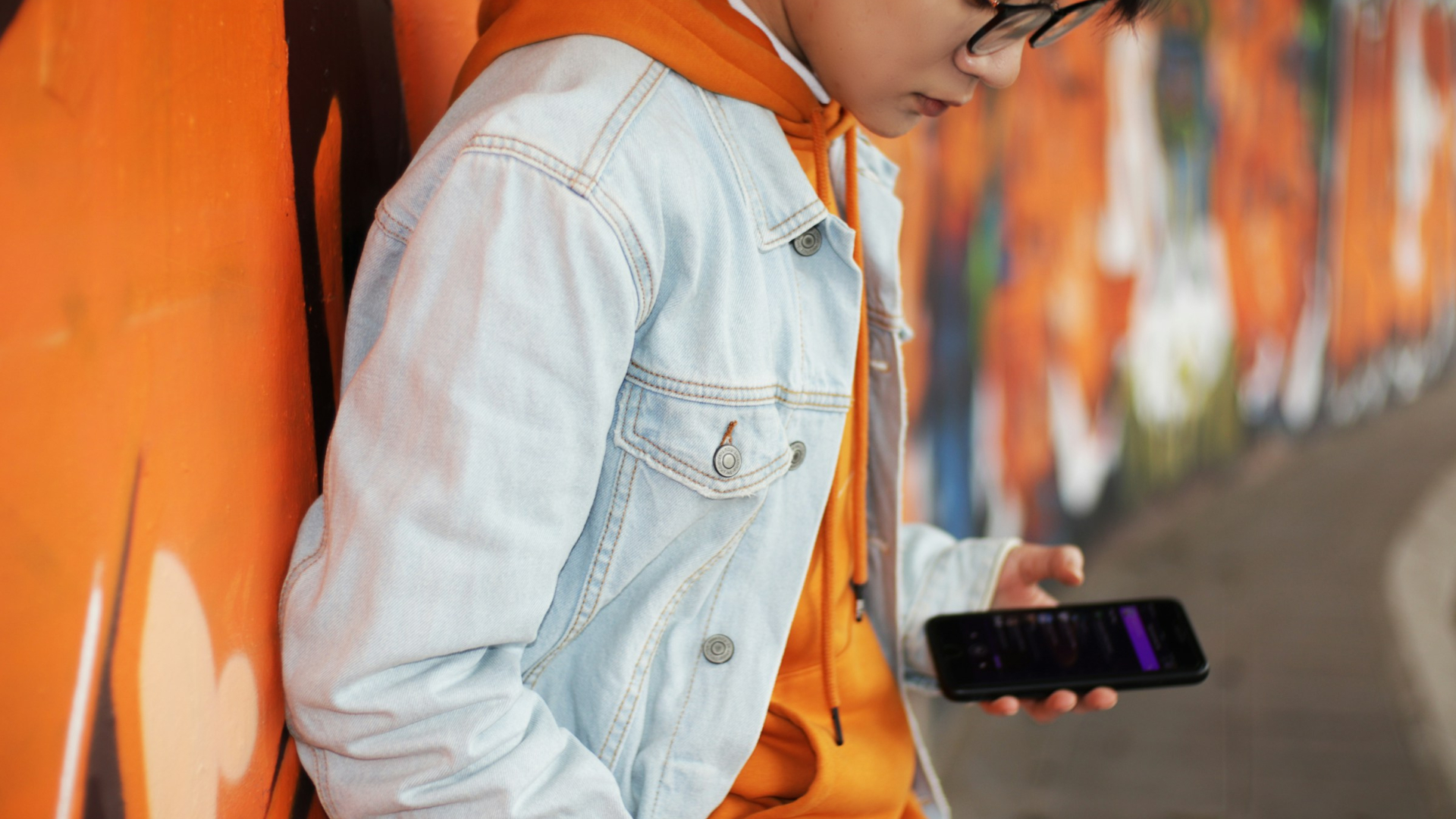 Jugendliche Person mit Smartphone vor Graffiti-Wand