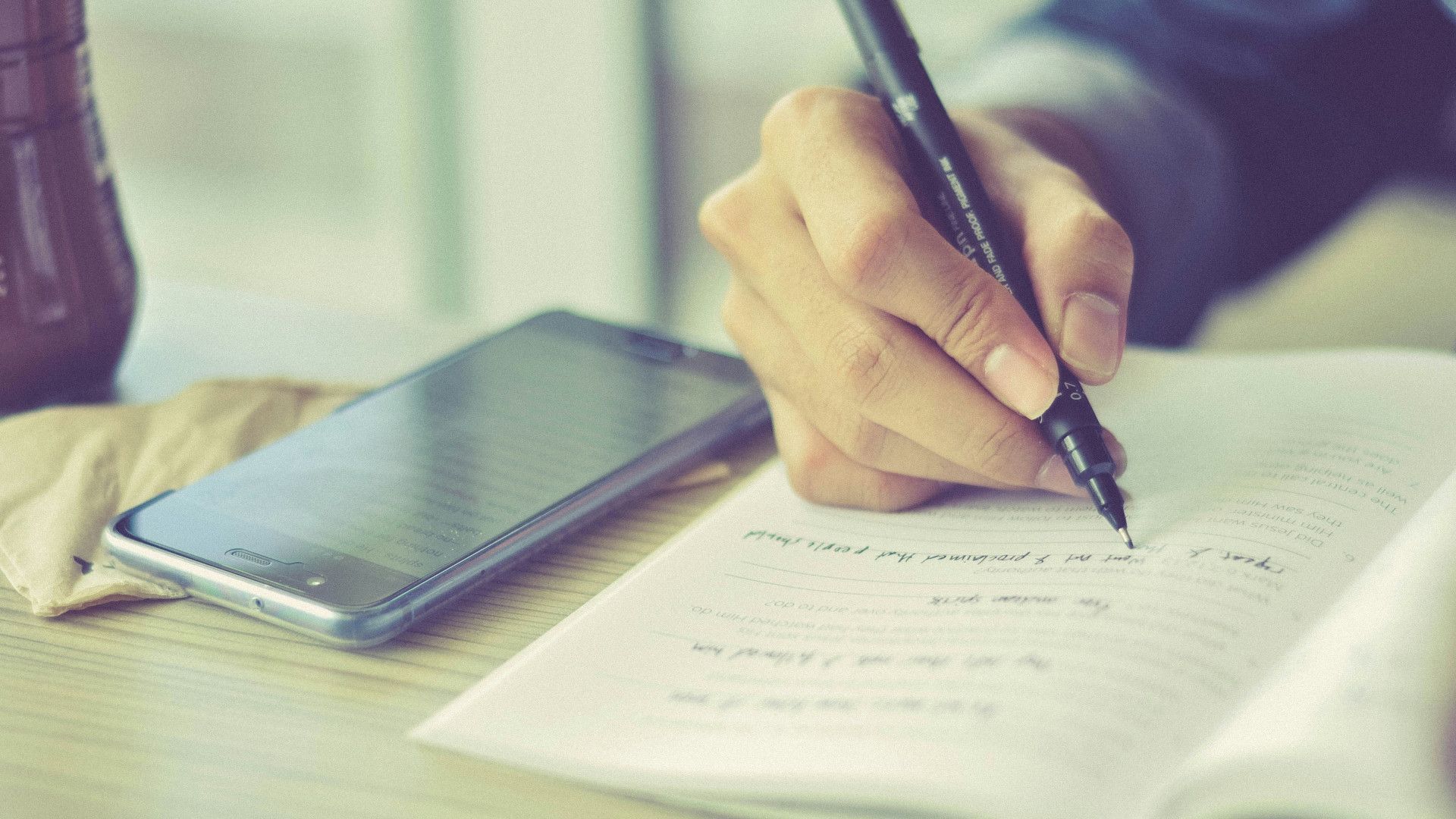 Smartphone auf einem Schultisch neben Schüler der in ein Heft schreibt