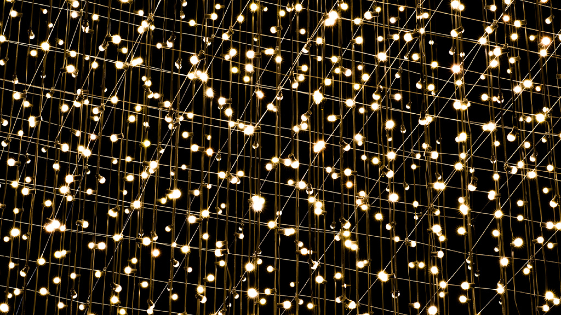 Künstlerisches Lichtnetz mit vielen warmweiß leuchtenden Punkten vor schwarzem Hintergrund.