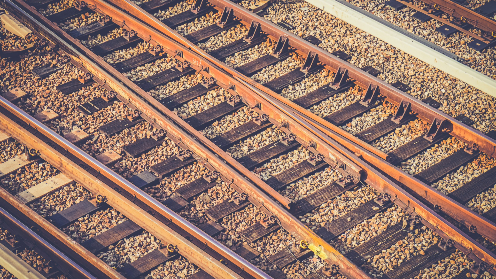 Mehrere rostbraune Eisenbahnschienen auf Holzschwellen im Schotter