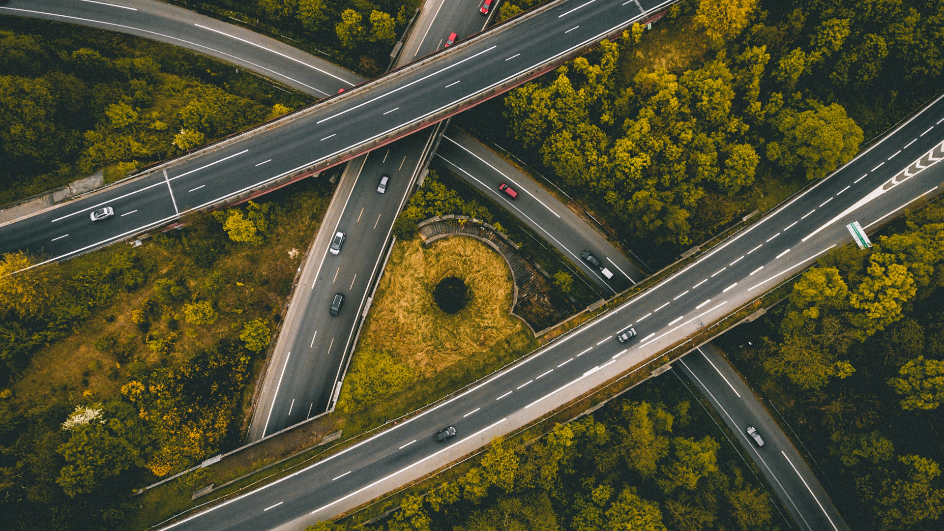Mehrspuriges Autobahnkreuz mit mehreren Autos, umgeben von dichtem grün-gelbem Wald.