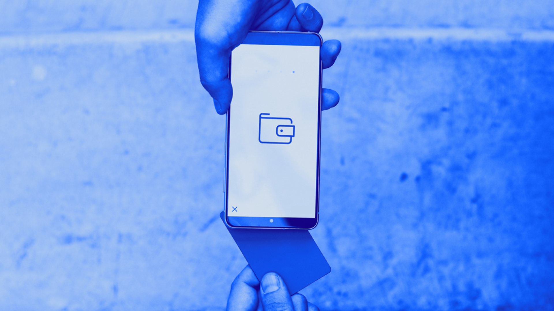 Jemand hält eine Karte in der Hand und legt diese an der Rückseite eines Handys an, das jemand anders in der Hand hält. Auf dem Handydisplay ist ein Wallet-Icon zu sehen. Das Bild zeigt einen digitalen, kontaktlosen Bezahlvorgang.