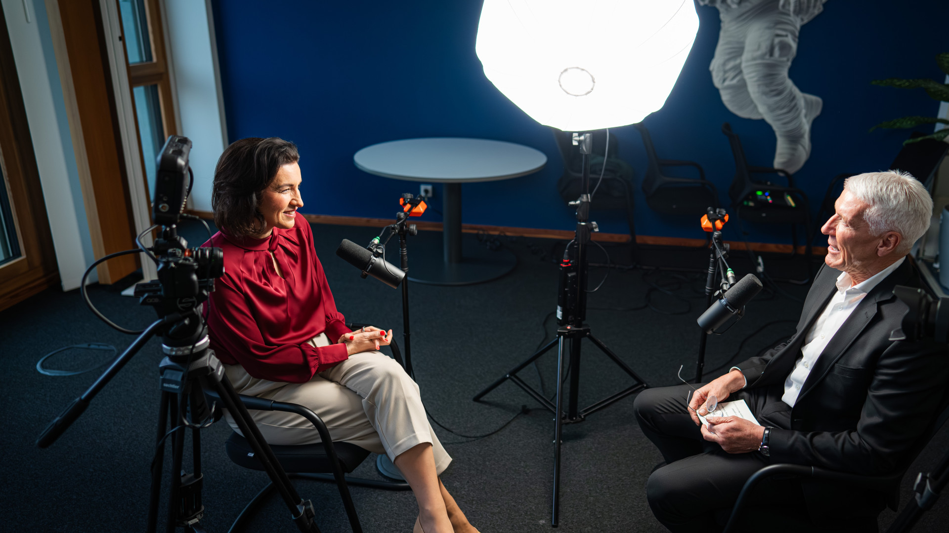 Zwei Personen im Interview: Dorothee Bär in rotem Oberteil, Ralf Wintergerst im schwarzen Anzug, beleuchtet von rundem Licht.