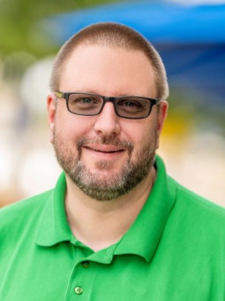 Torsten Hallmann, mit grauen Haaren und Bart, trägt ein grünes Polohemd und Brille, lächelt frontal zur Kamera.