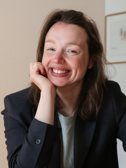Julia Kowalski, eine Frau mit langen, braunen Haaren, sitzt in einem hellen Raum und lächelt.