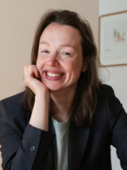 Julia Kowalski, eine Frau mit langen, braunen Haaren, sitzt in einem hellen Raum und lächelt.