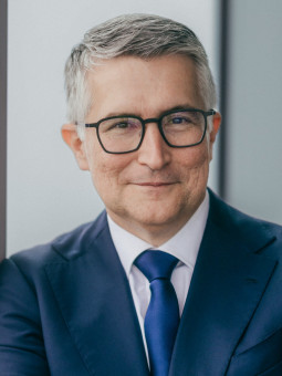 Mann mit grauen Haaren in blauem Anzug und Krawatte, lächelt, steht an einer Glaswand. Text: "Santiago Argelich-Hesse", "c: Telefonica".