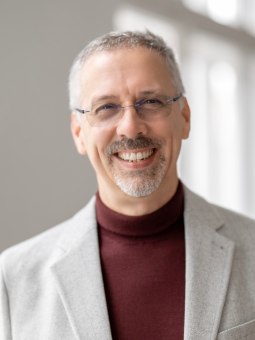 Chris Hendriks - Speaker DSS 2026. Mann mit grauen Haaren, Brille, grauem Blazer und burgunderfarbenem Rollkragenpullover.