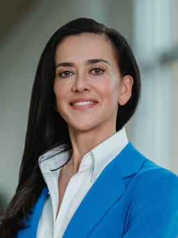 Person in blue suit and white shirt standing with arms crossed in a bright, modern interior with wooden floor.