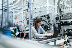 Frau sitzt in Industriewerkstatt am Laptop