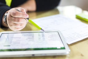 Person sitzt vor einer Rechnung vor Papier und einem Tablet