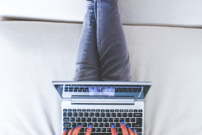 Frau sitzt auf Couch und arbeitet am Laptop