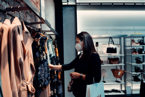 Frau mit Maske steht im Geschäft vor einer Kleiderstange