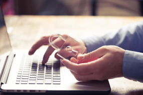 Am Laptop arbeitende Hände, eine Hand hält Glasschloss