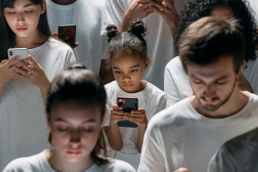 Personen verschiedener Ethnien und Altersgruppen stehen und schauen auf ihre Smartphones. Alle tragen weiß. 