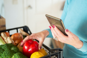Frau mit Smartphone und Einkaufskorb gefüllt mit Obst und Gemüse
