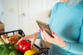 Frau mit Smartphone und Einkaufskorb gefüllt mit Obst und Gemüse