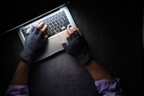  Hände in fingerlosen Handschuhen tippen am Laptop, dunkle Atmosphäre 