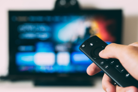 Fernbedienung vor verschwommenem Flachbildfernseher mit Kacheln auf dem Bildschirm