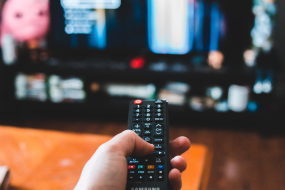 Person sitzt mit Fernbedienung vor einem Fernseher