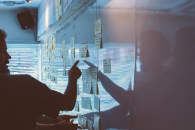 Eine Person steht vor einem Whiteboard, an dem mehrere Post-its kleben.