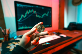 Hand mit Bitcoin-Münze vor Trading-Monitor