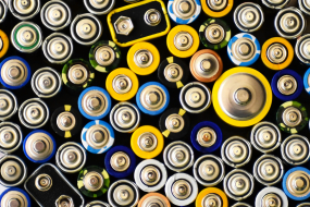 Dicht angeordnete Batterien in verschiedenen Größen und Farben, von oben auf ihre Pole fotografiert.