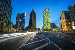 Abendaufnahme vom Potsdamer Platz mit beleuchteten Hochhäusern und Lichtspuren fahrender Autos.
