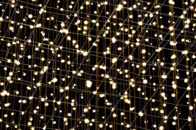 Künstlerisches Lichtnetz mit vielen warmweiß leuchtenden Punkten vor schwarzem Hintergrund.
