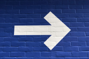 Weißer Pfeil zeigt nach rechts auf blauer Ziegelwand.