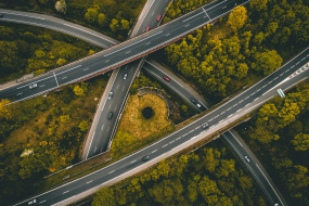 Mehrspuriges Autobahnkreuz mit mehreren Autos, umgeben von dichtem grün-gelbem Wald.