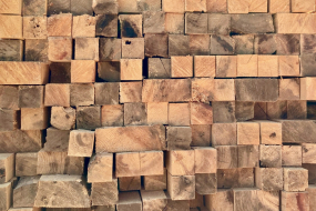 Unbehandelte, quadratische Holzbalken liegen gestapelt mit sichtbaren Maserungen.