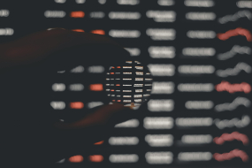 Eine Hand hält eine Linse vor einen unscharfen Datenbildschirm.