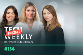 Drei Frauen stehen nebeneinander, jede in unterschiedlichen Oberteilen. Hintergrund unscharf, Text in der linken unteren Ecke.