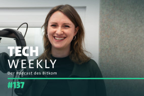 Lächelnde Frau mit langen, braunen Haaren, schwarzem Oberteil und Kopfhörern vor grauer Wand. Text: "TECH WEEKLY Der Podcast des Bitkom #137".