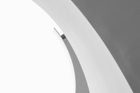 Kurve in einem hellen, minimalistischen Raum mit neutralem Grauton und einem kleinen dunklen Bereich.