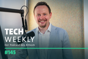 Person in hellem Anzug lächelt vor Mikrofon. Hintergrund mit strukturierter Wand. Text: "TECH WEEKLY", "Der Podcast des Bitkom", "#145".