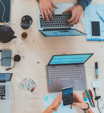 Schreibtisch mit vielen Laptops und Händen von Personen die gemeinsam arbeiten