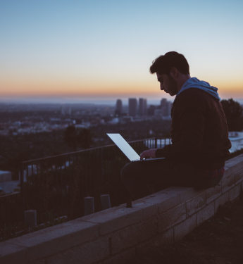 Junger Mann sitzt mit Laptop über den Dächern einer Stadt